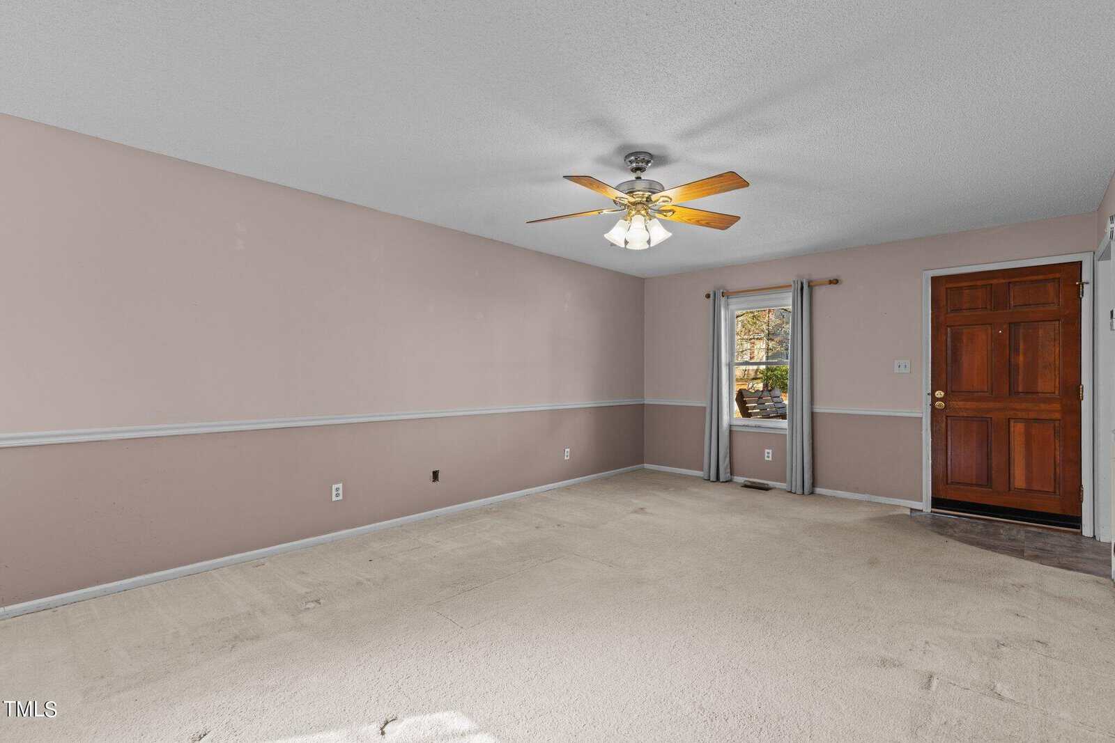 An empty room with pink walls, a ceiling fan, carpeted flooring, and a sliding door leading outside.