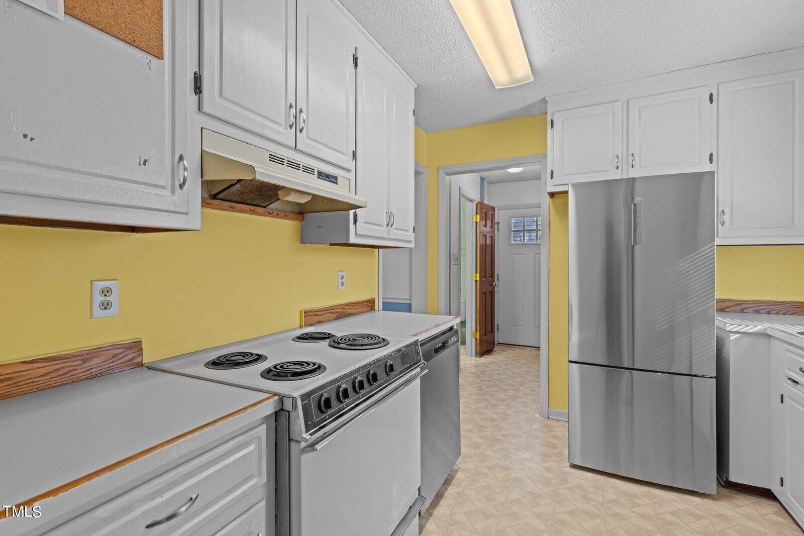 A kitchen interior with white cabinetry, yellow walls, a white refrigerator, and an older model electric range.