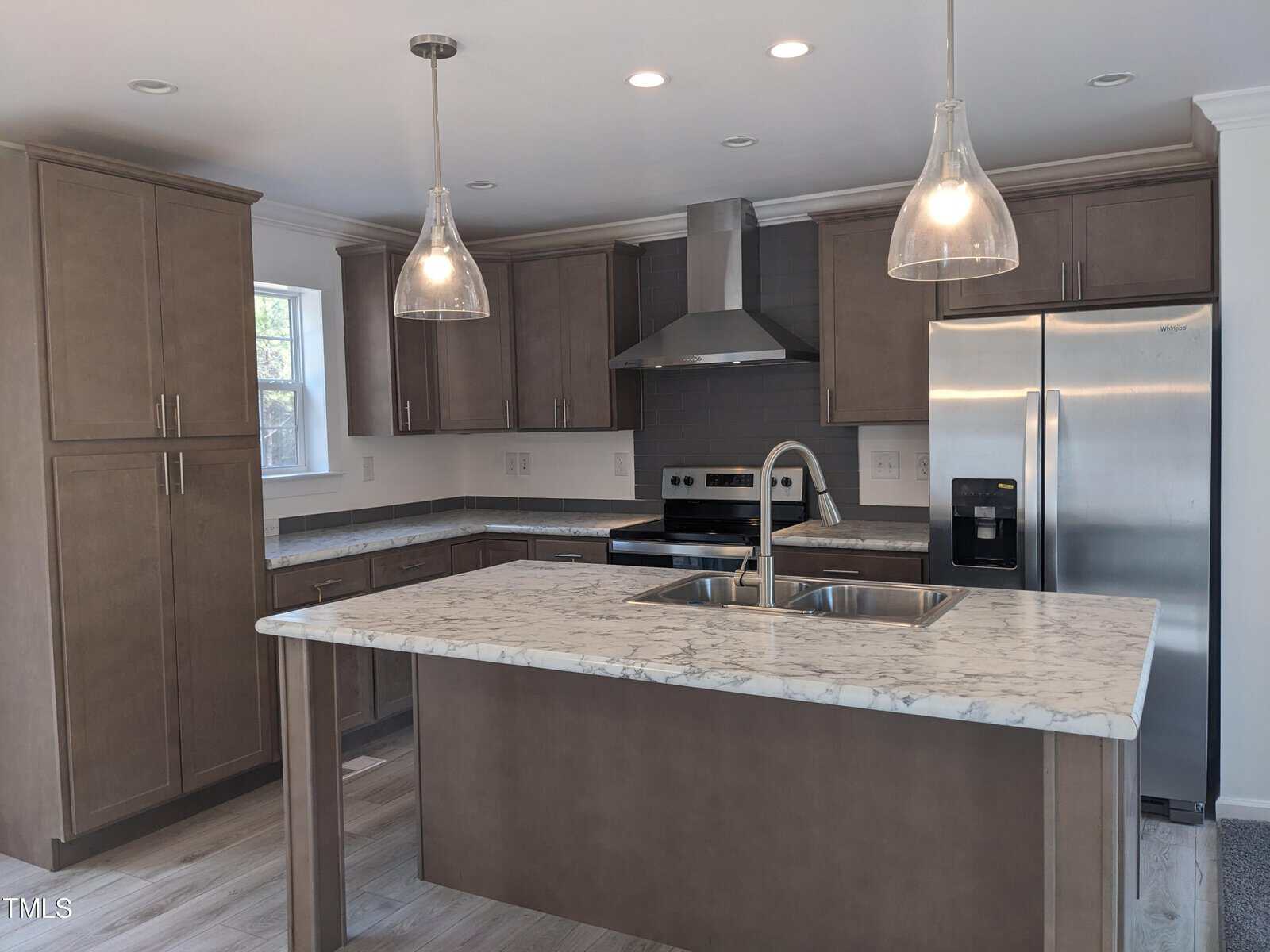 A modern kitchen with gray cabinetry, marble countertops, stainless steel appliances, and pendant lighting over an island.