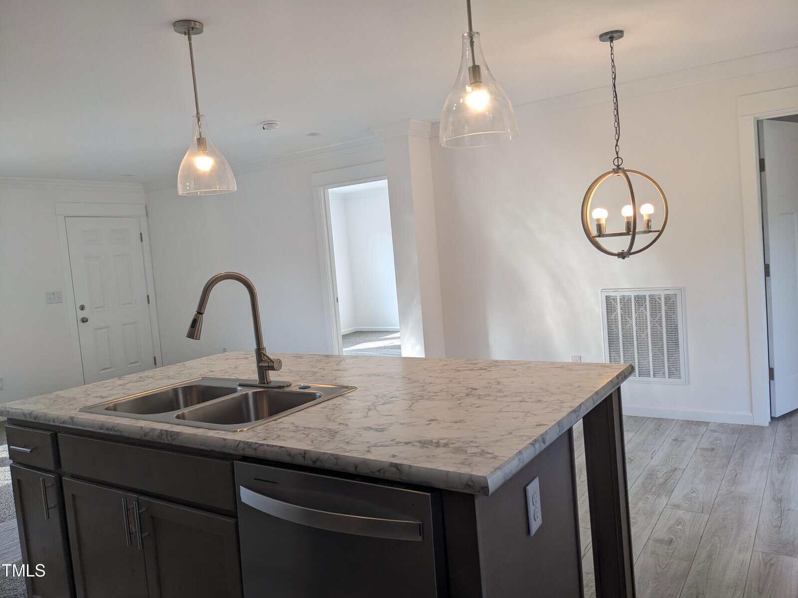 A modern kitchen featuring a dark gray island with a marble countertop and a built-in sink, pendant lights above, and a view of white doors and a bright interior.