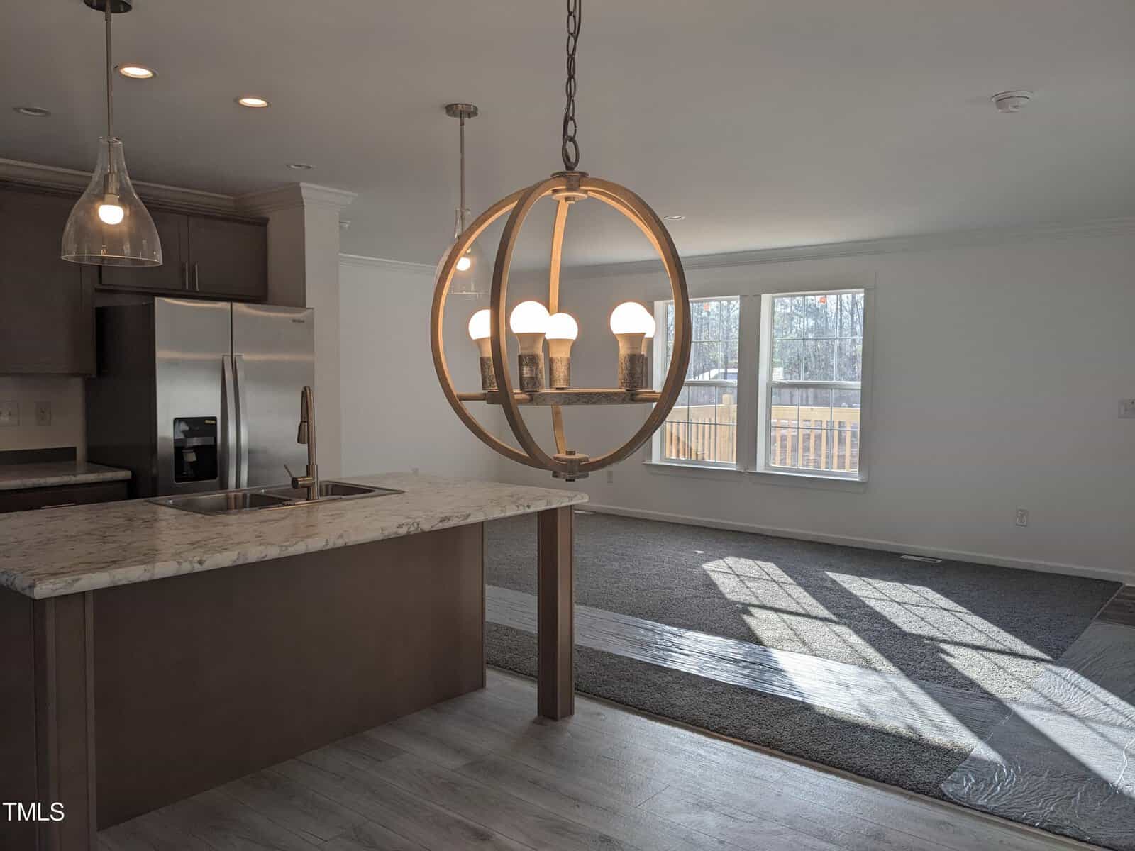A modern kitchen featuring a marble island, stainless steel appliances, and gray cabinets, adjacent to a living area with hardwood flooring and a large window.