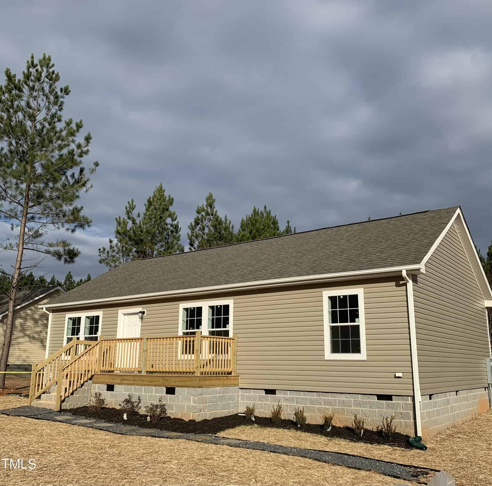 A new beige single-story house at 447 Plum Nutty Road, Henderson NC, with a small wooden porch and steps, located in a freshly landscaped area with bits of grass and several small shr