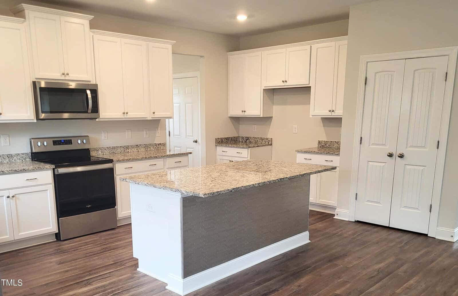 Modern kitchen with white cabinets, stainless steel appliances, and granite countertops. Features a central island with storage, hardwood floors, and recessed lighting. Double-door pantry is visible in the background.