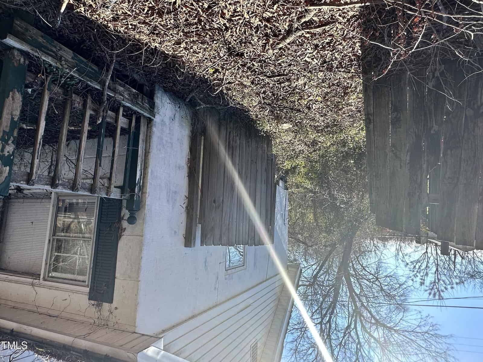 An upside-down image of a weathered house with peeling paint, overgrown vines, and boarded-up windows under a clear blue sky.