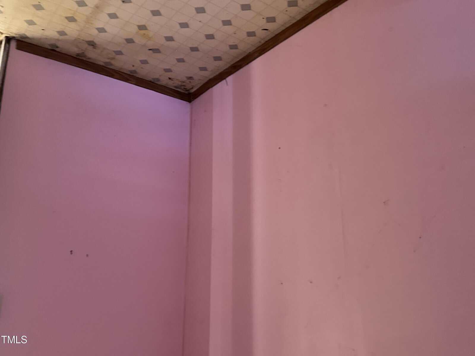 A corner of a room with pink walls and a partially visible ceiling with square tiles.