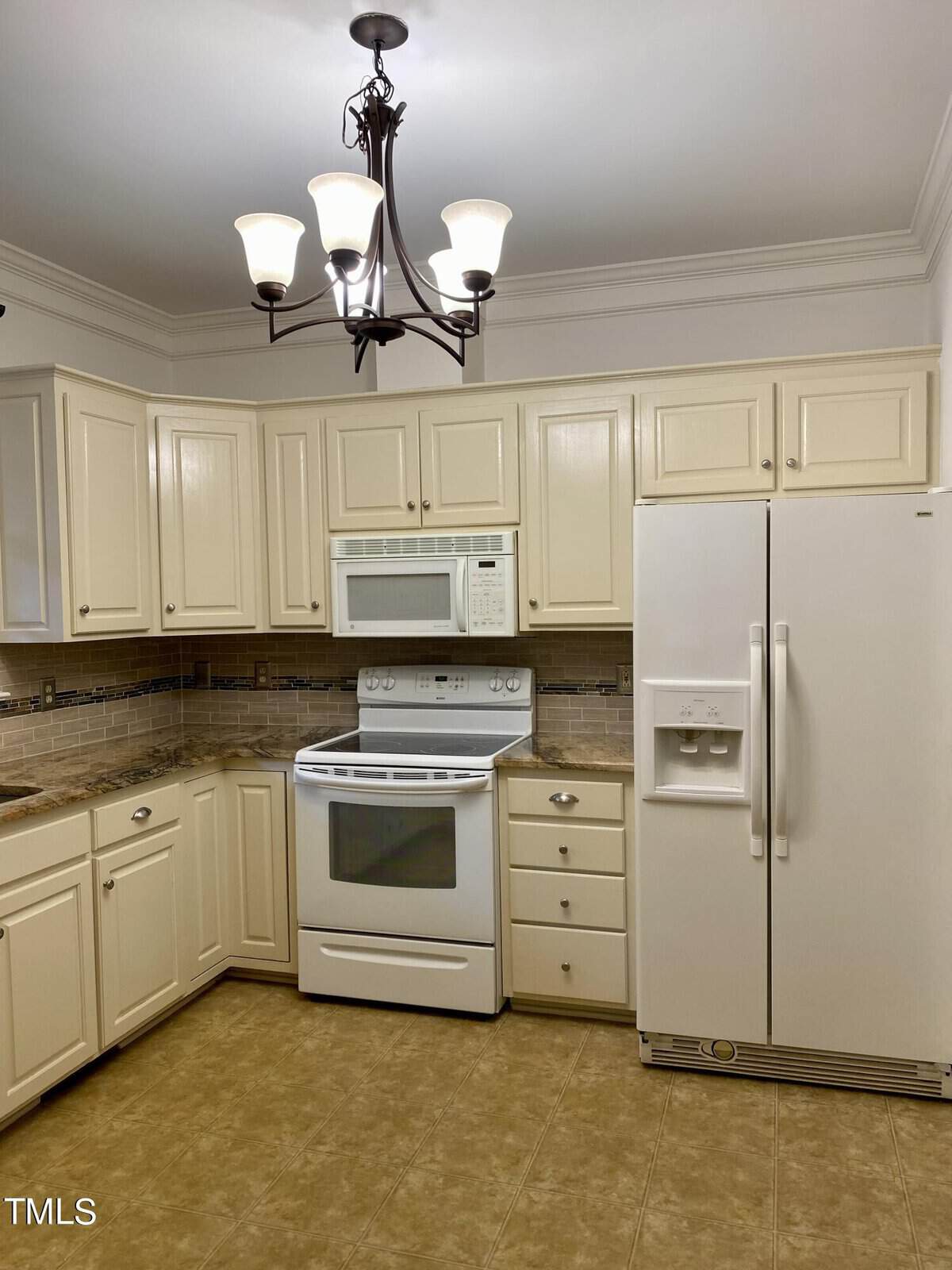 A well-lit kitchen with off-white cabinets, dark countertops, a white refrigerator, and an electric range.