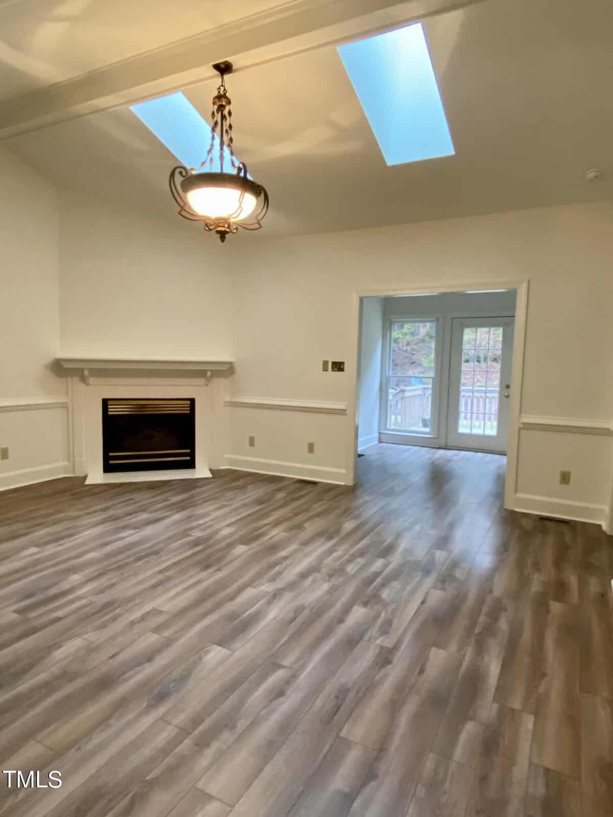 An empty room featuring a fireplace, hardwood floors, skylights, and a glass door leading to an outdoor balcony.