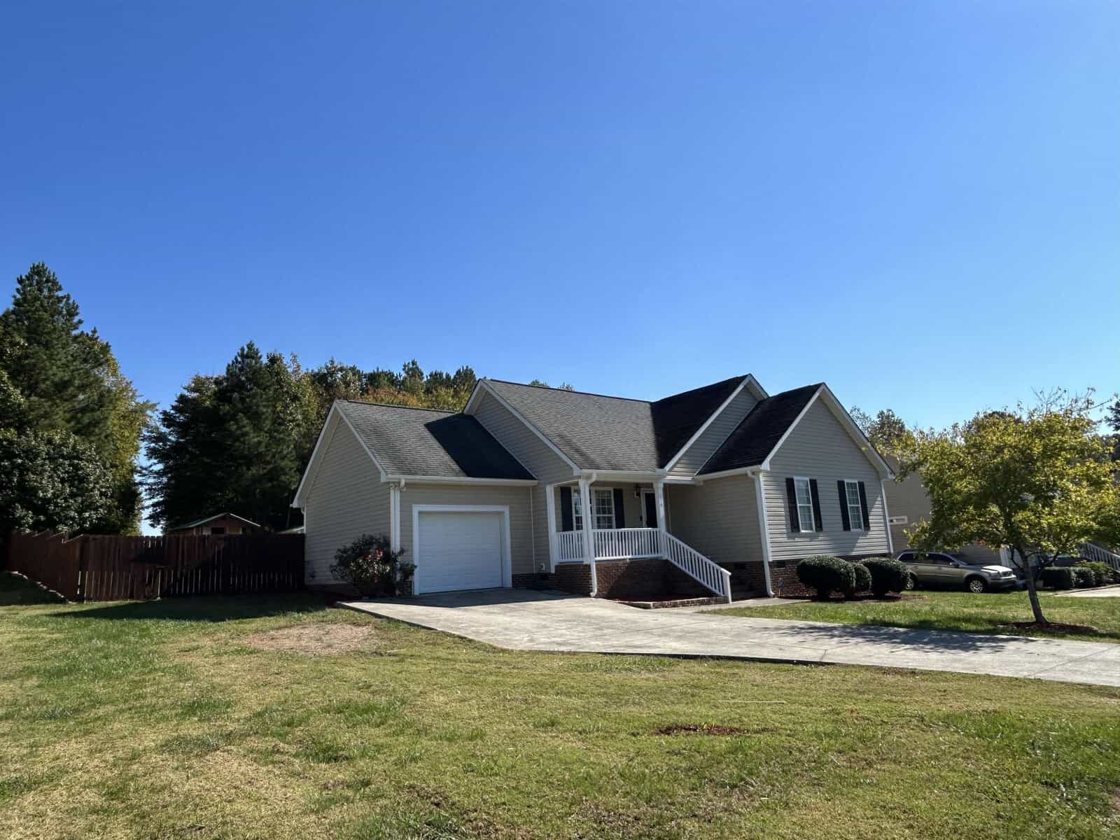 Located at 110 Carriage Hill Drive, this charming single-story house boasts light-colored siding and a dark roof. With a welcoming front porch, attached garage, and a driveway that stems from the street, it's nestled amid grassy lawns and trees under the clear blue sky.