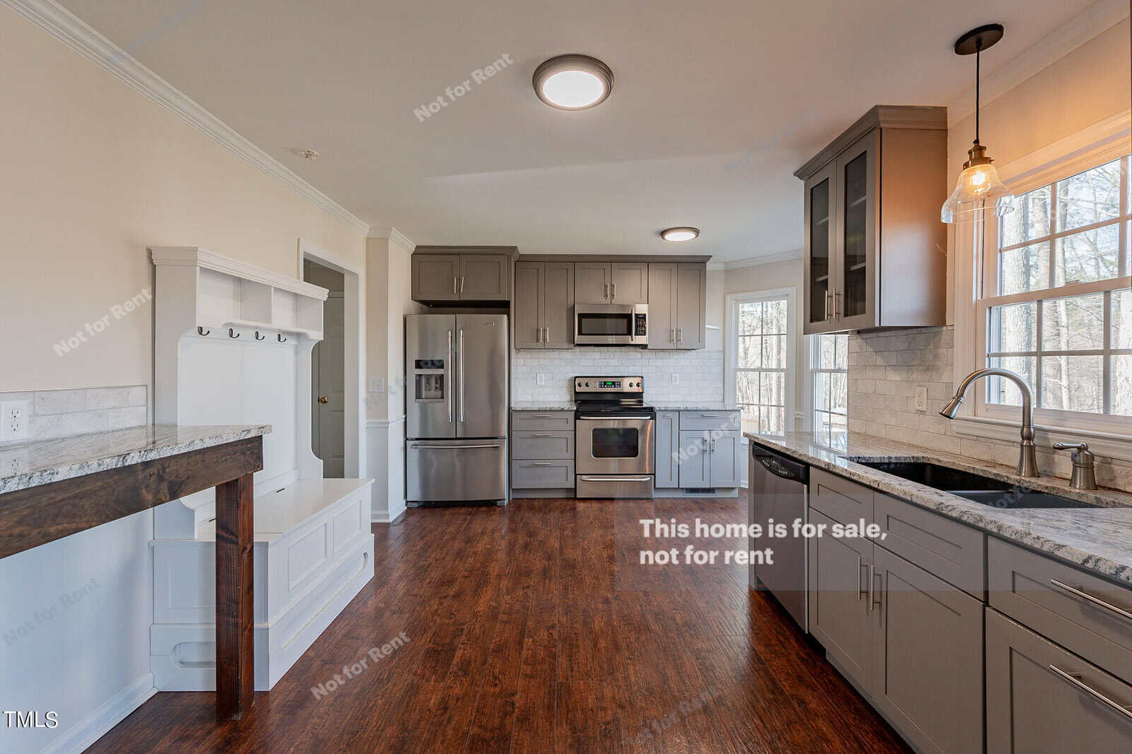 Modern kitchen with gray cabinets, stainless steel appliances, and hardwood floors. A large window provides natural light. A breakfast bar with marble countertop is on the left, and a pendant light hangs above the sink.