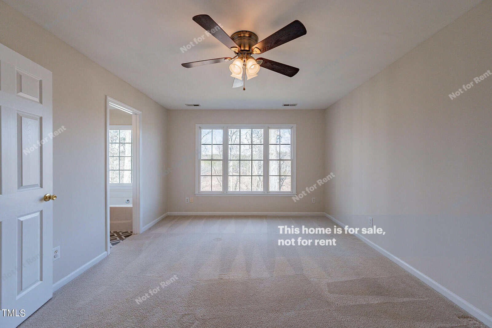 An empty room with beige carpet, cream walls, and a ceiling fan with lights. Two large windows allow natural light. A door on the left is slightly open. Text on the image reads, "This home is for sale, not for rent.