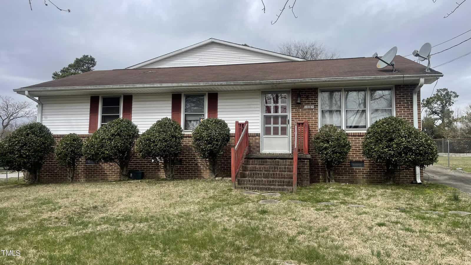 Located at 207 Summitt Avenue, this charming Oxford single-story brick house features a red shingle roof and white siding. Adorned with red shutters, it has a central entrance with steps, bushes lining the front, and two satellite dishes on the right. The grassy lawn completes the serene setting under an overcast sky.