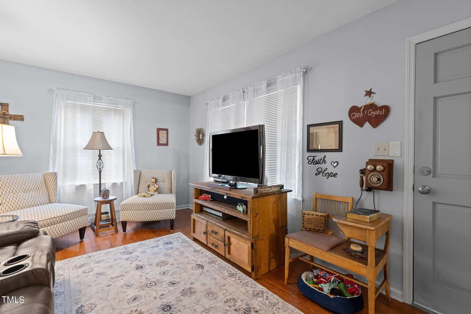 A cozy living room with a television on a wooden stand, a striped sofa, an armchair, and decorative items on the walls and surfaces.