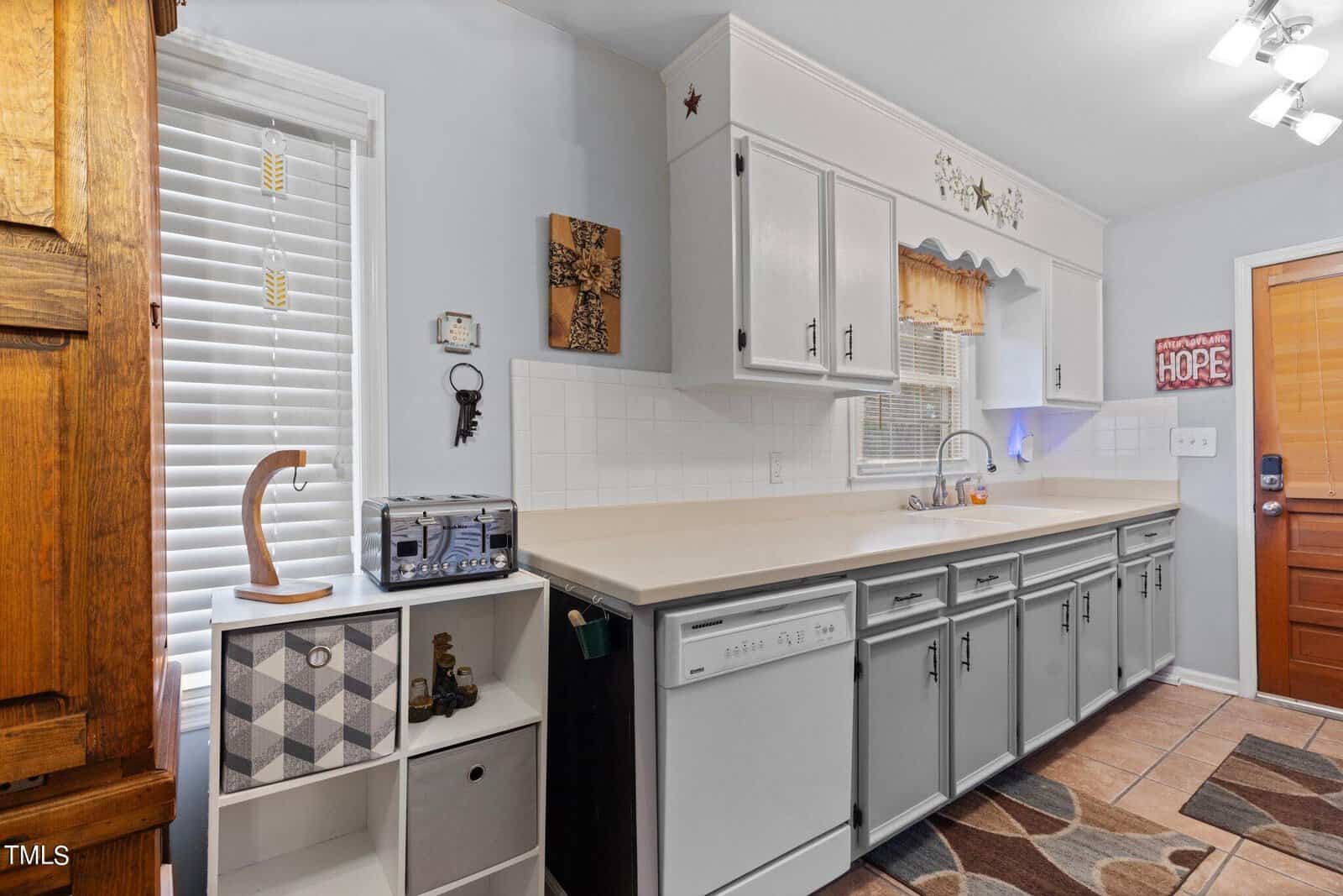 A tidy, well-organized kitchen with white cabinetry, tile backsplash, and modern appliances, featuring a decorative chess-themed corner shelf and various wall adornments.
