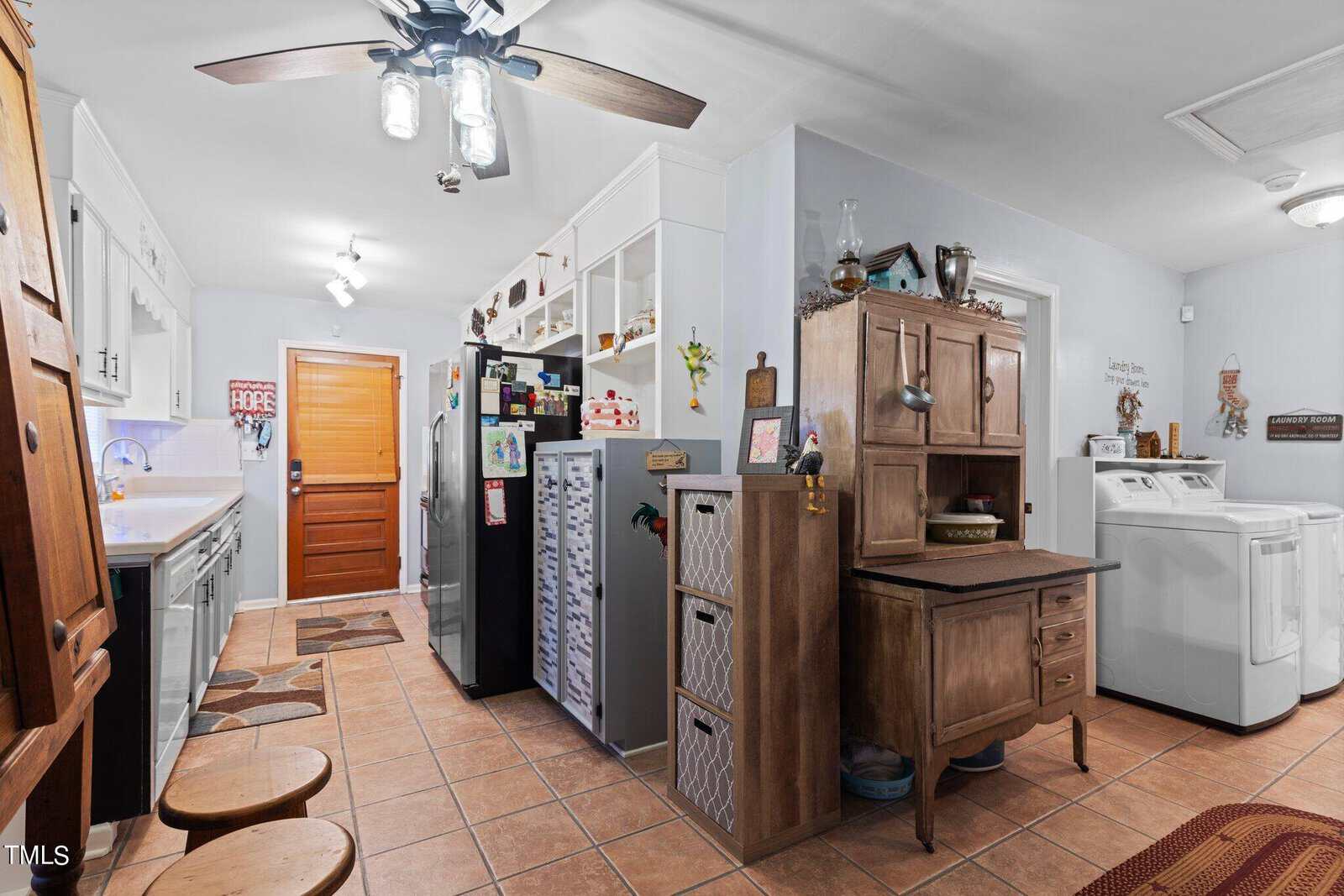 A spacious kitchen with white cabinets, a central wooden island, modern appliances, and a tiled floor, featuring a ceiling fan and ample lighting.