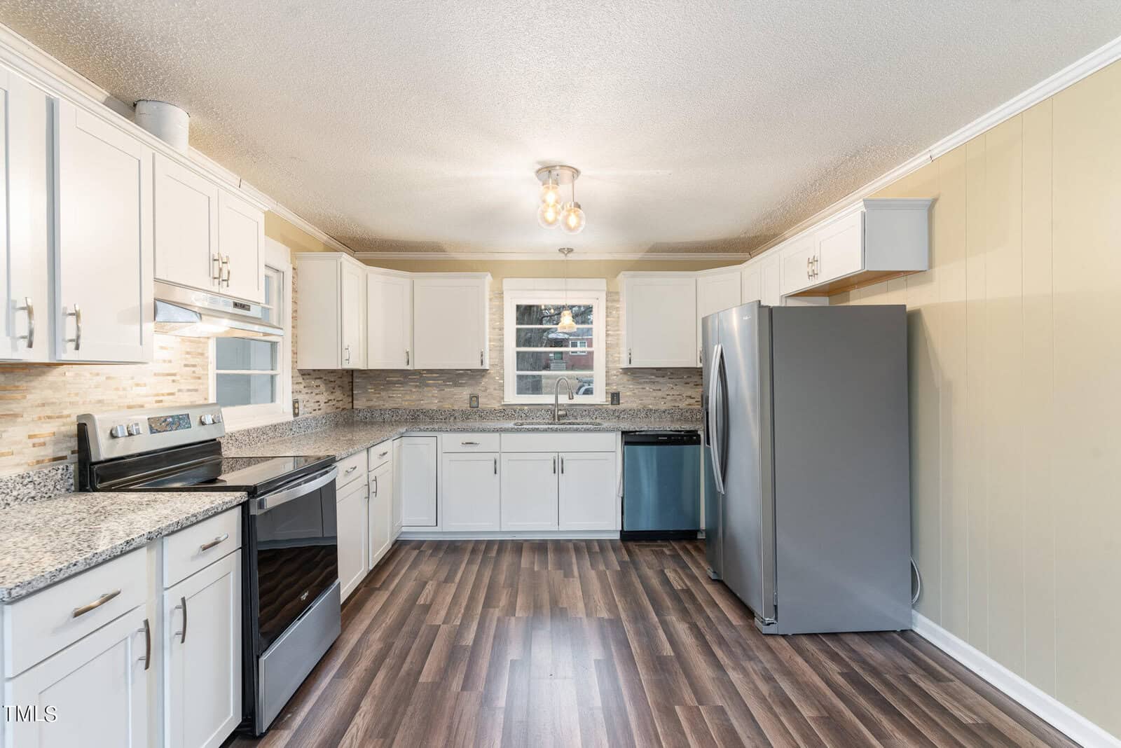 A modern kitchen interior featuring white cabinetry, stainless steel appliances, a multicolored backsplash, and wooden flooring under white ceiling lights.