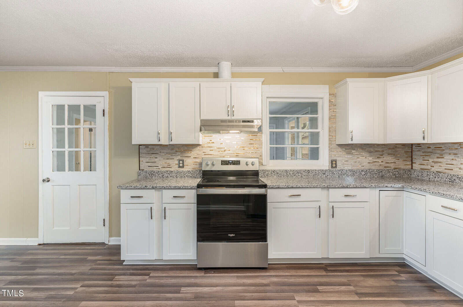 A modern kitchen with white cabinetry, granite countertops, and stainless steel appliances, featuring a wooden floor and a door with glass panels.
