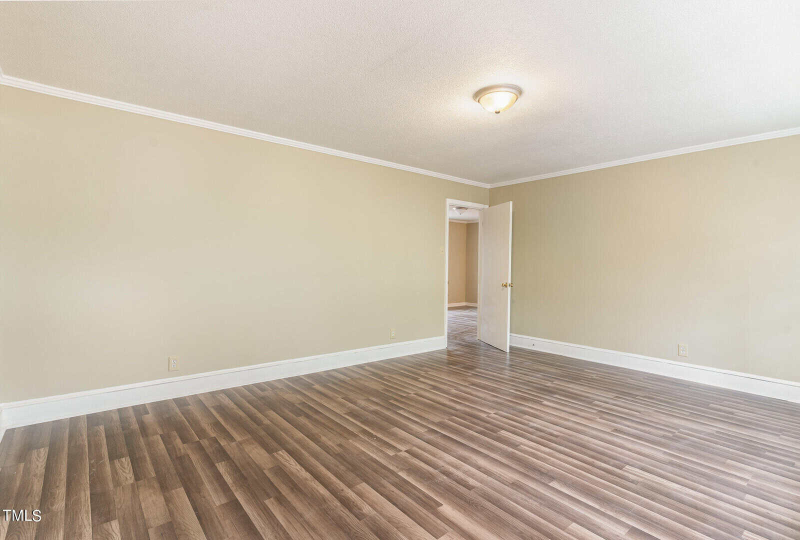 Empty room with pale yellow walls, dark brown wood flooring, and a white open door leading to another room. a basic light fixture is on the ceiling.