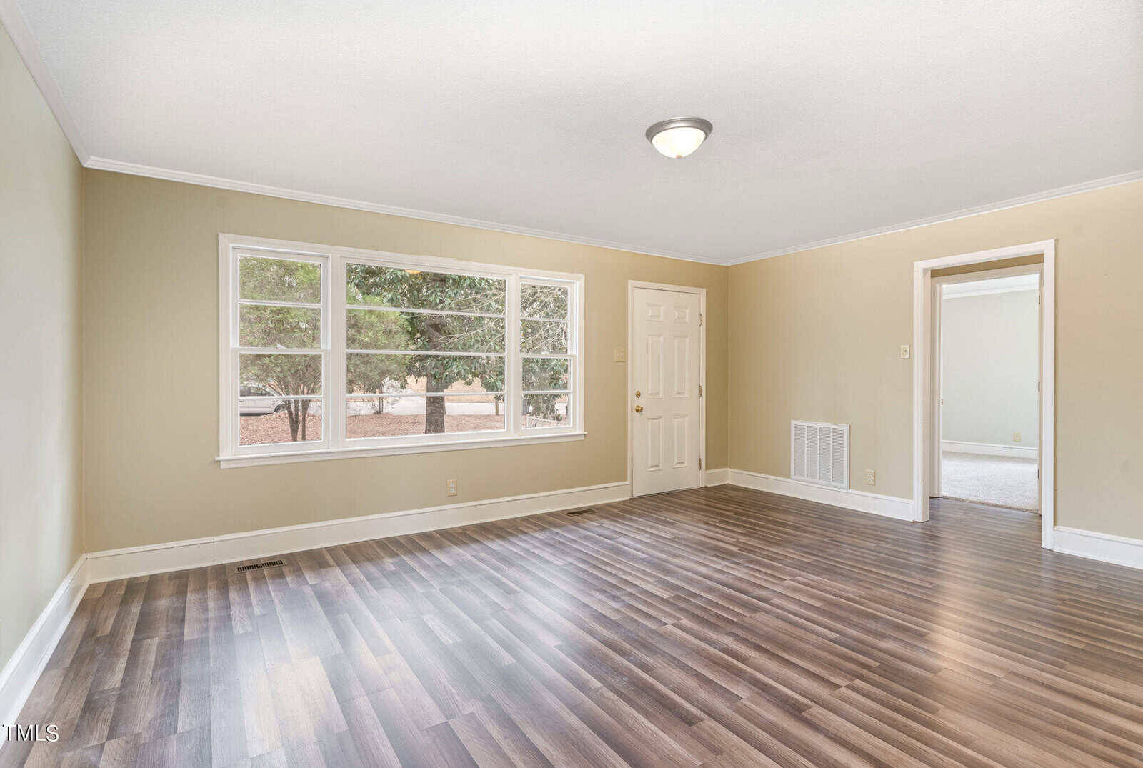 Empty room with glossy hardwood floors, green walls, a white door, and a large window looking out to trees. there's a single light fixture on the ceiling.