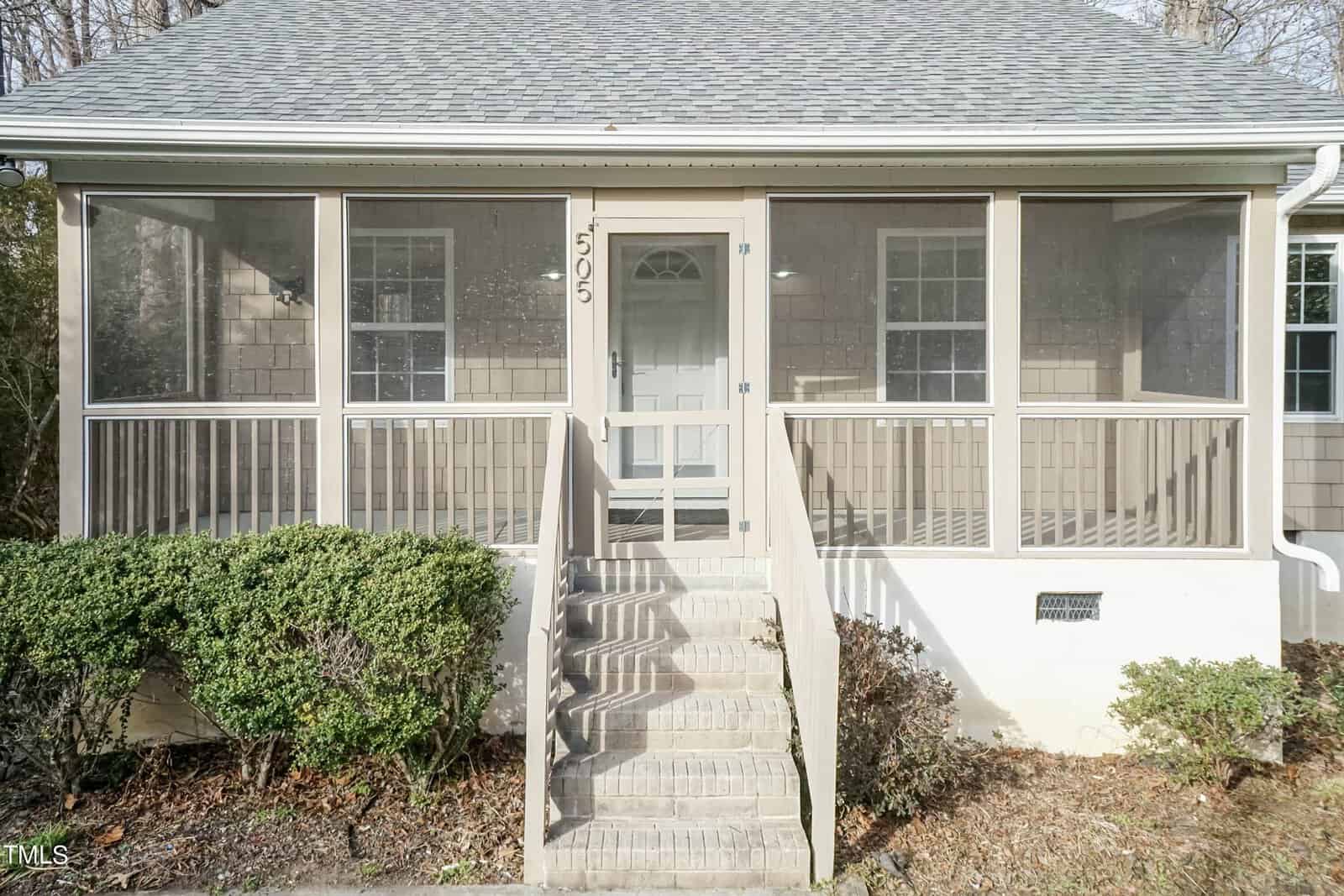 The image shows the front view of a house with a screened-in porch. The porch has stairs leading up to it, bordered by shrubs on either side. The number "505" is displayed above the front door.