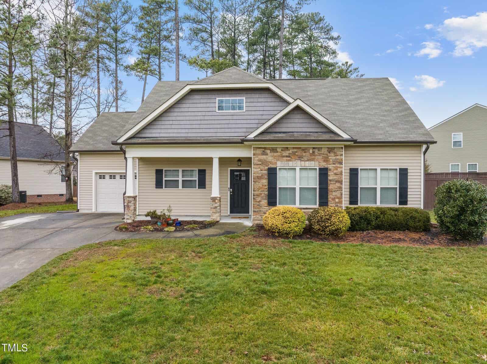 Nestled at 113 Griffis Drive, this cozy one-story house boasts a gray roof and stone accents. With white siding, a black front door, and an attached garage, it's surrounded by a well-manicured lawn with trees in the background. The clear blue sky completes this inviting scene in Stem.