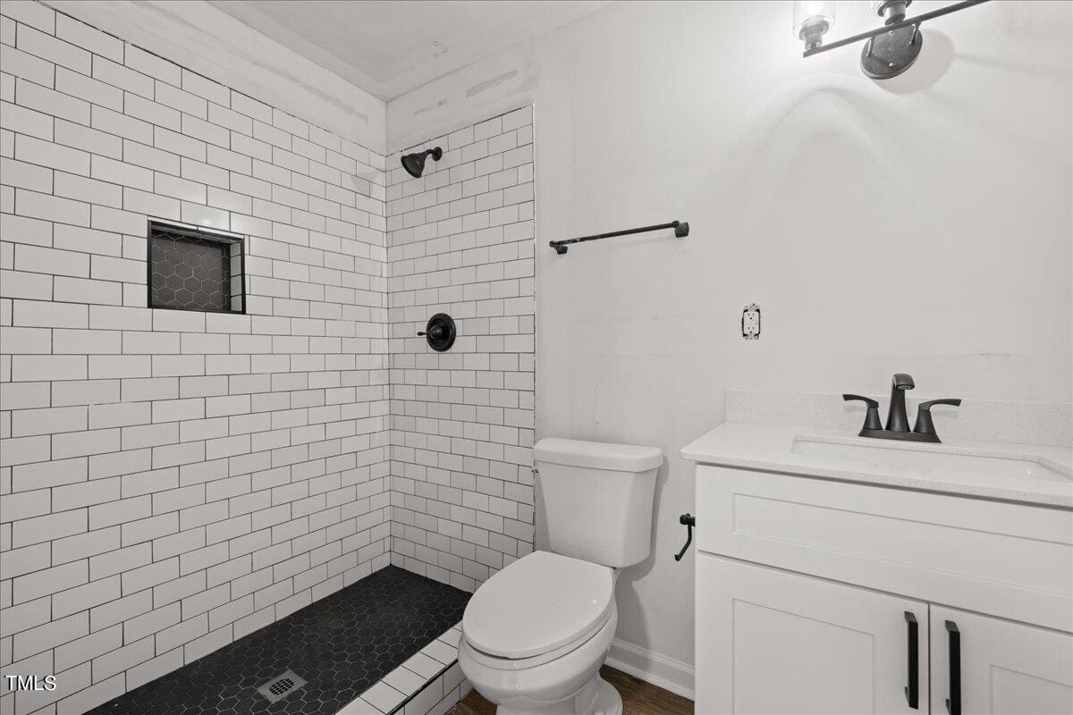 A modern bathroom featuring white subway tiles on the walls, a small frosted window, a white vanity with a sink, a toilet, and black hexagonal floor tiles. there's a wall-mounted light fixture above the mirror.