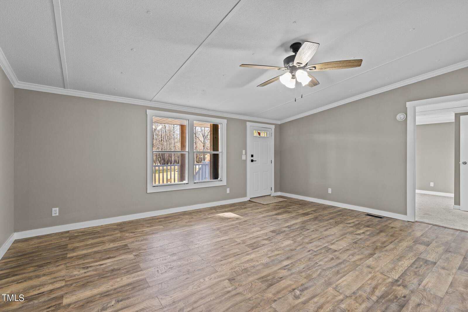 A spacious, empty room with wood laminate flooring, grey walls, a white ceiling with a mounted fan, windows providing natural light, and a door leading to a balcony.