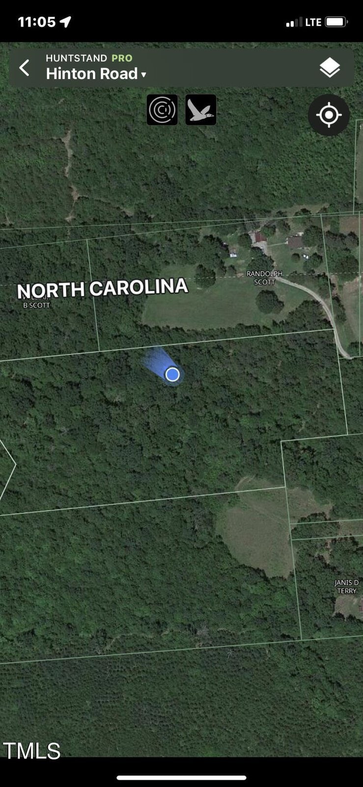 A satellite map view displaying a forested area in North Carolina. The location is marked in the center with a blue dot, surrounded by green trees. Nearby roads and residential outlines are visible, with Hinton Road as a highlighted location.