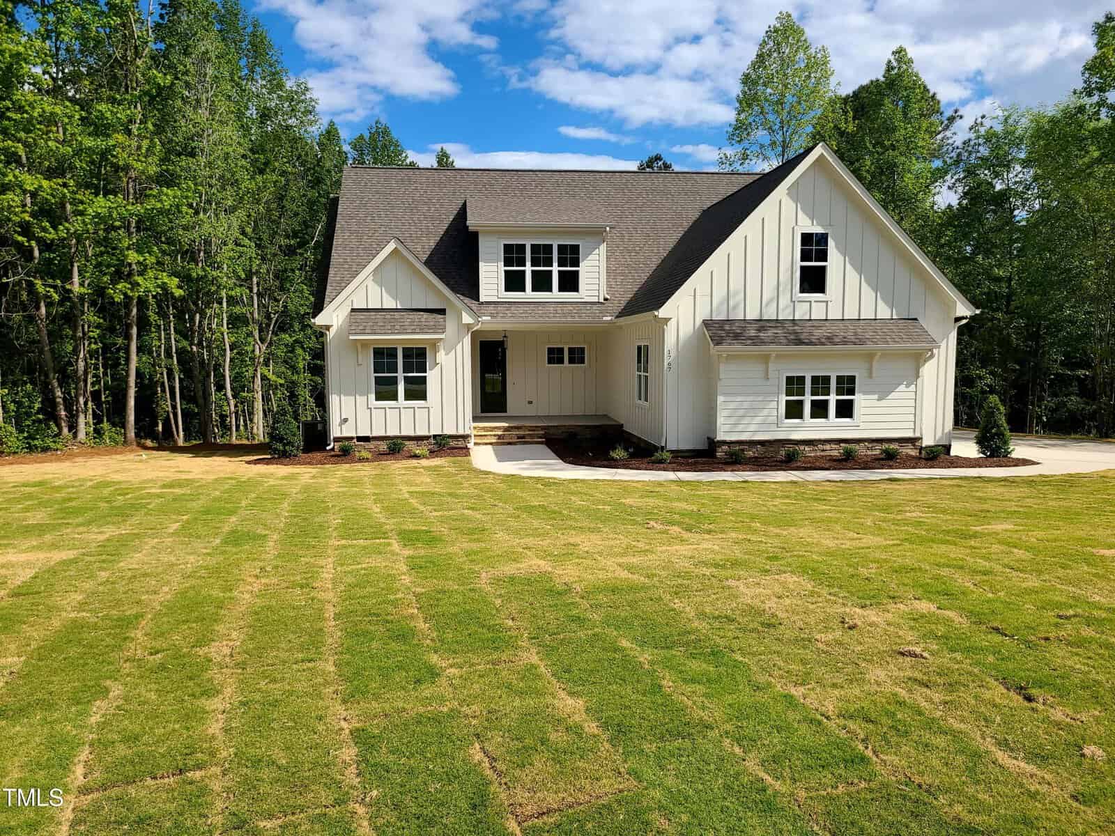 Nestled in Franklinton, this modern beige two-story house at 1767 River Club Way features a steep gray roof, a lush green lawn, and is bordered by tall trees under a partly cloudy blue sky.
