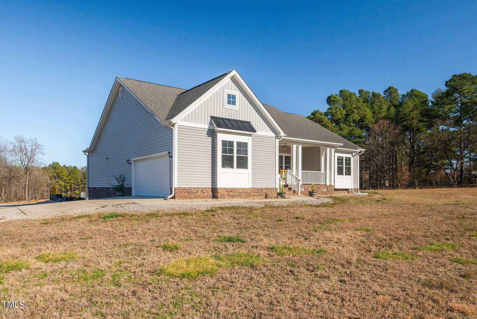 A single-story, modern suburban home with a gray siding exterior and white trim, set on a large plot of land with sparse grass under a clear sky.