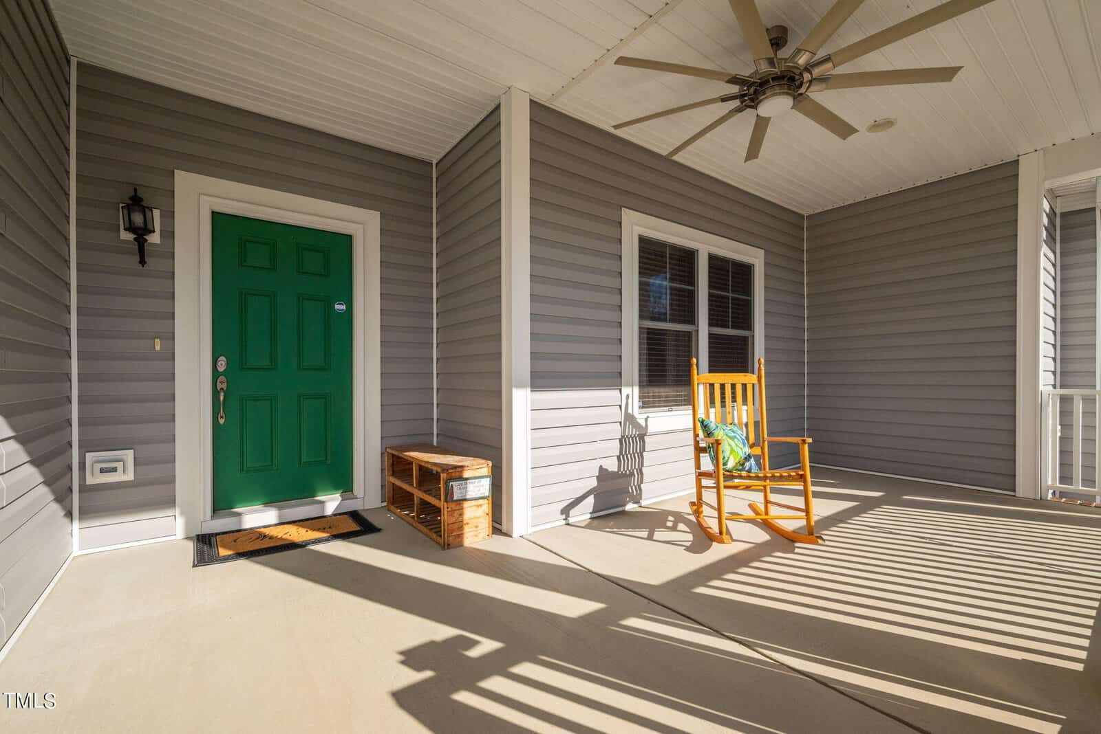 A sunlit porch with a bright green door and a single wooden rocking chair. shadows of the porch railing cast long, dramatic lines on the floor.