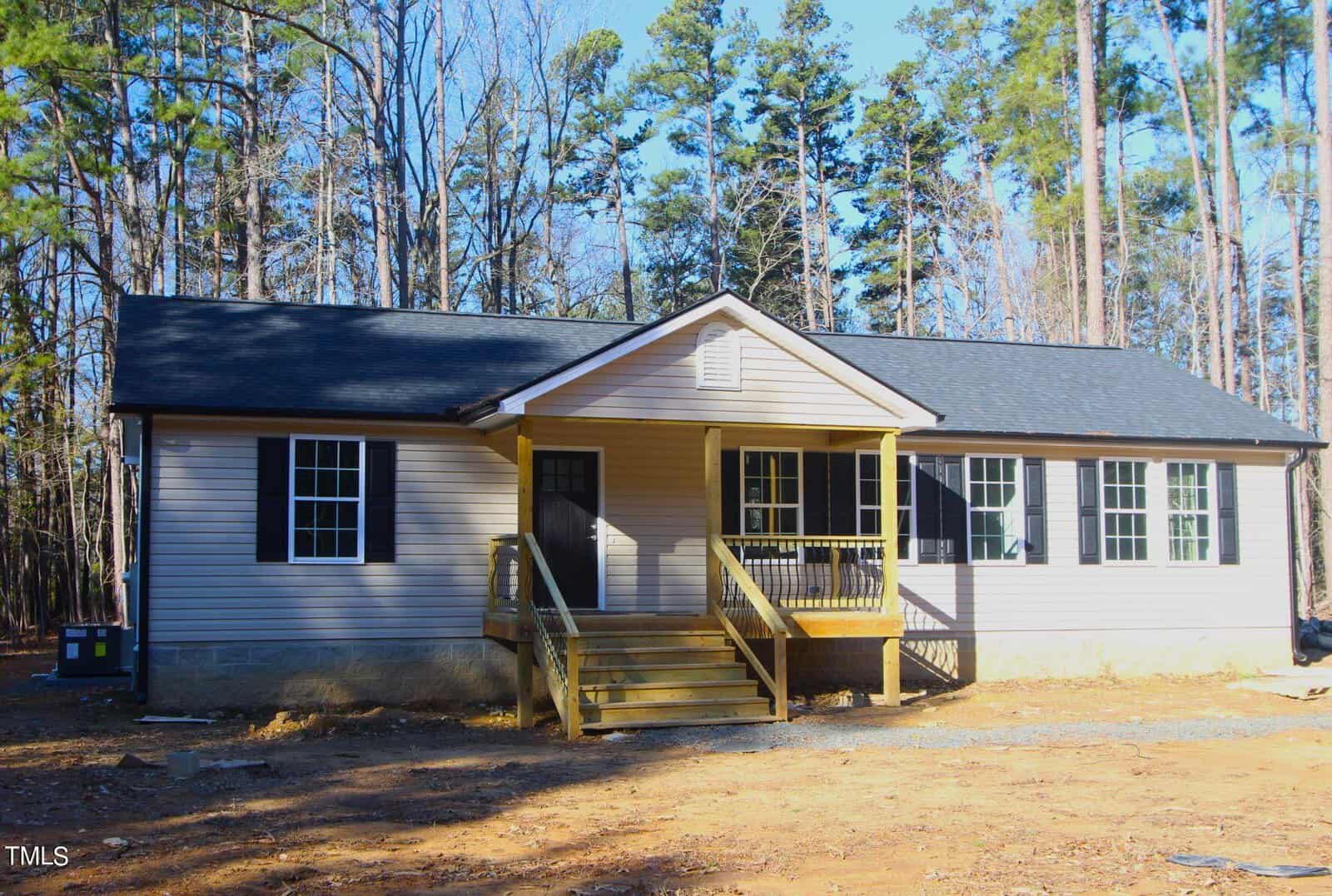 Nestled in the heart of Oxford, this small, single-story house with a beige exterior and black roof is surrounded by tall trees. Located at 6609 US Hwy 15, it boasts a wooden porch with steps leading to the front door, letting sunlight filter through the cleared area around it.