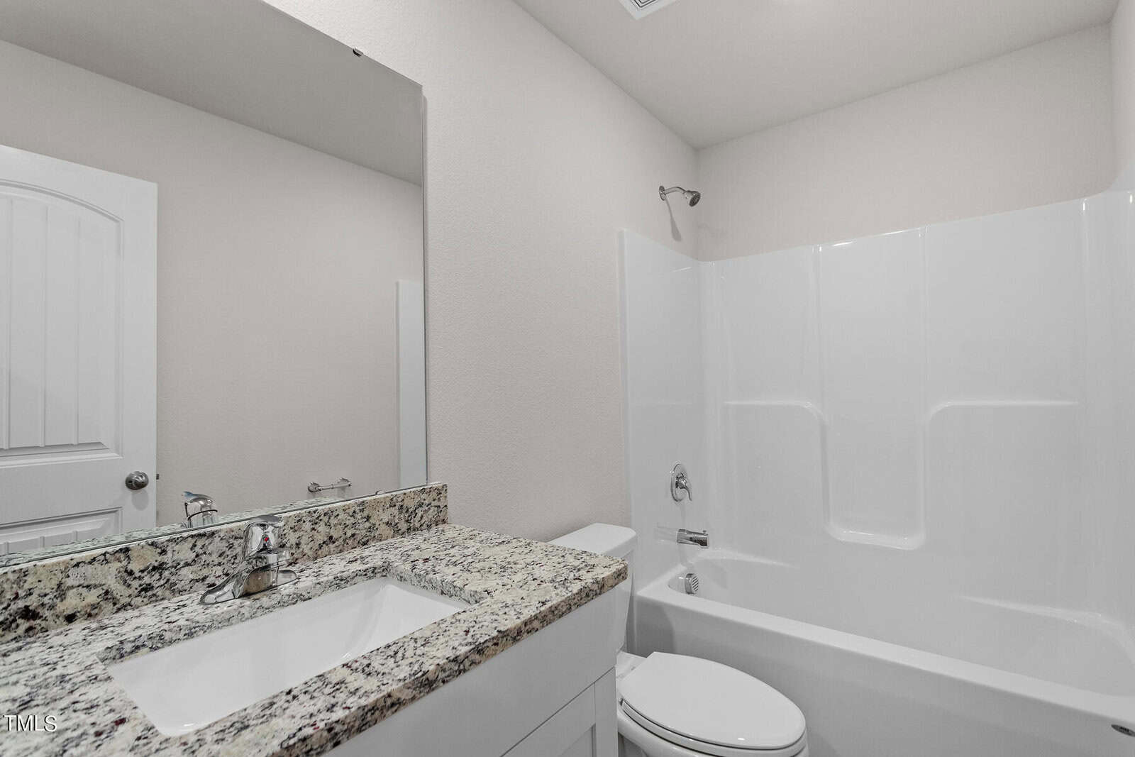 Modern bathroom featuring a marble countertop with a rectangular sink and chrome faucet. A large mirror is mounted above the sink. The room includes a white bathtub with an integrated shower, and a white door is visible on the left.