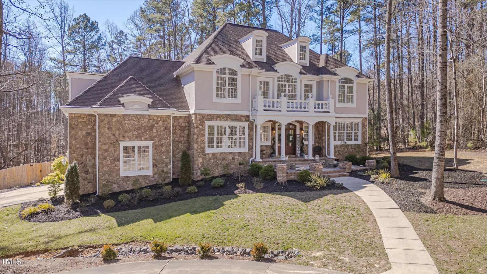 Located at 1061 Silverleaf Drive in Youngsville, this large, elegant two-story house features a stone and stucco exterior, multiple dormer windows, and a covered front porch. A well-maintained lawn and tall trees surround it, with a curved driveway leading to the entrance.