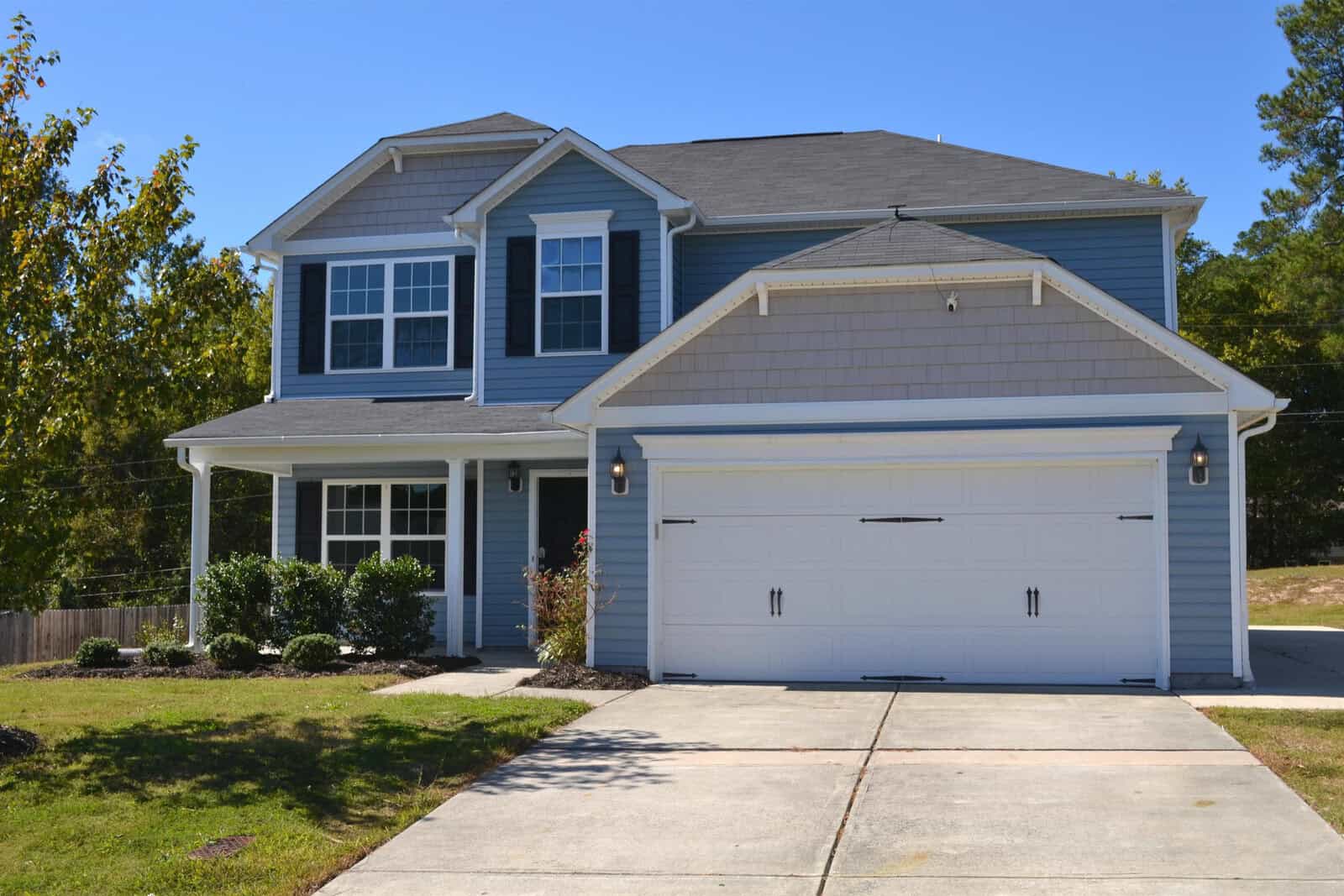 Nestled at 710 Pitch Pine Drive in Creedmoor, this modern two-story house features a blue exterior with white trim and a spacious garage. The well-maintained lawn and concrete driveway complete the charming setting against a backdrop of trees under a clear blue sky.