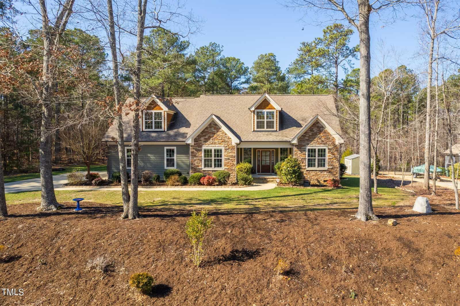 Nestled at 1501 Anterra Drive in Wake Forest, this beautiful, large house features stone and beige siding. Surrounded by bare trees and a landscaped lawn, it boasts dormer windows on the roof and a central double front door, with a paved driveway gracefully curving around it.