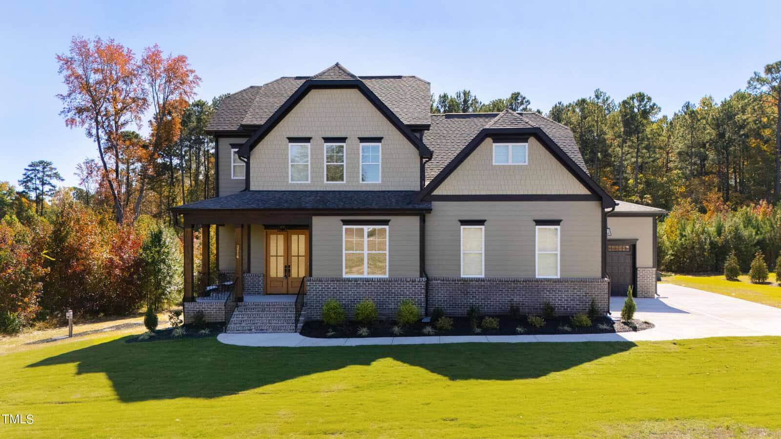The charming two-story house at 3216 Bruce Garner Road in Creedmoor boasts a gabled roof and a welcoming front porch, all set against a neatly landscaped lawn. Its exterior showcases light-colored siding and brickwork, with the backdrop of trees displaying vibrant autumn foliage.