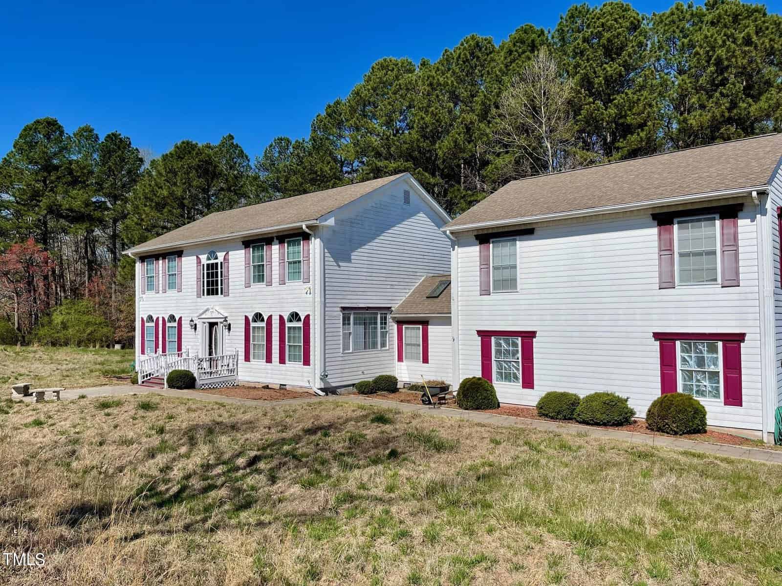 A two-story residential building at 101 Ber Lake Drive, Henderson NC, with a white facade and red accents, features a central section with a columned porch flanked by two wings, set amidst