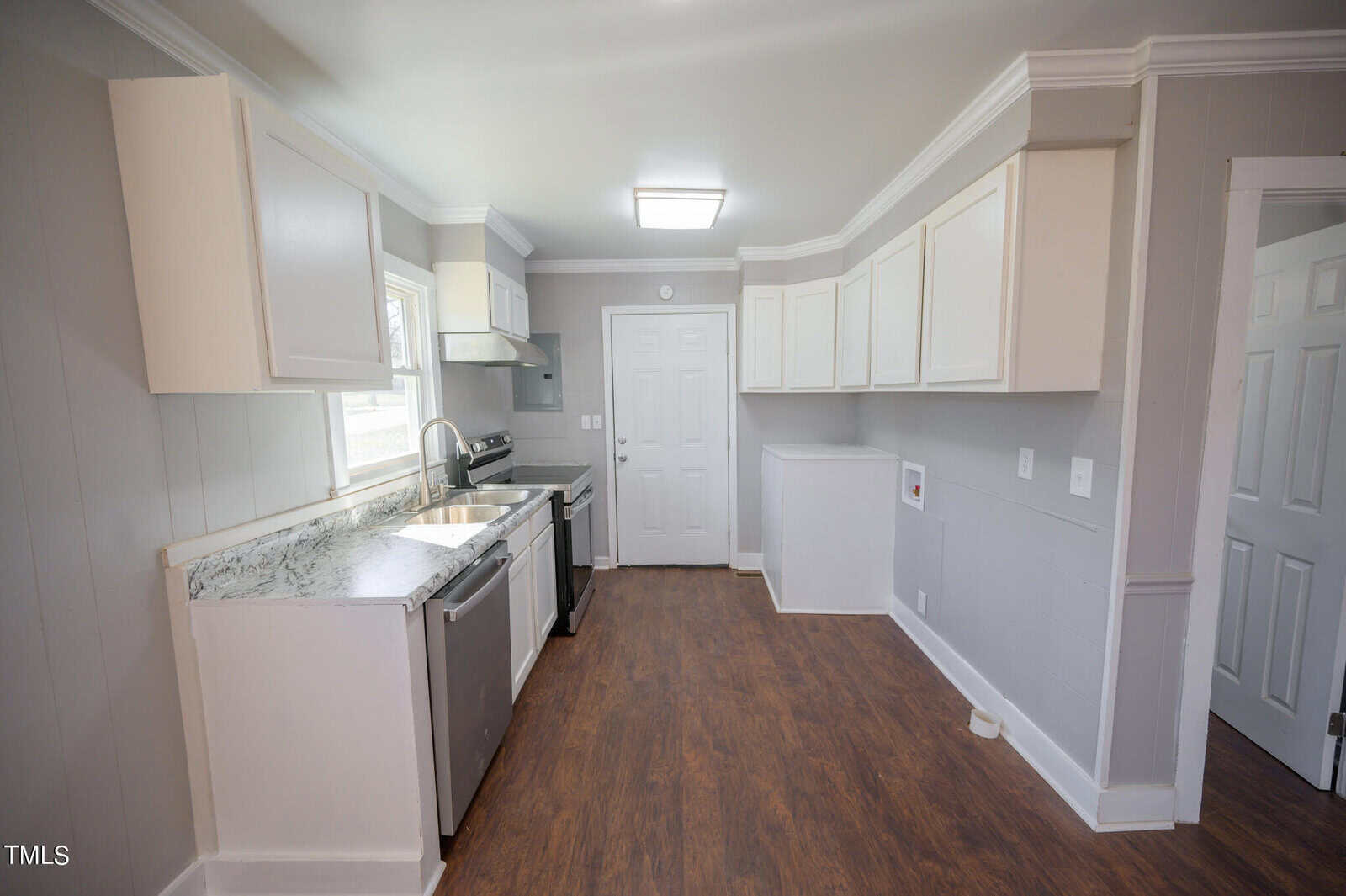 A modern kitchen with white cabinetry, dark countertops, and wooden flooring. includes stainless steel appliances and a back door.