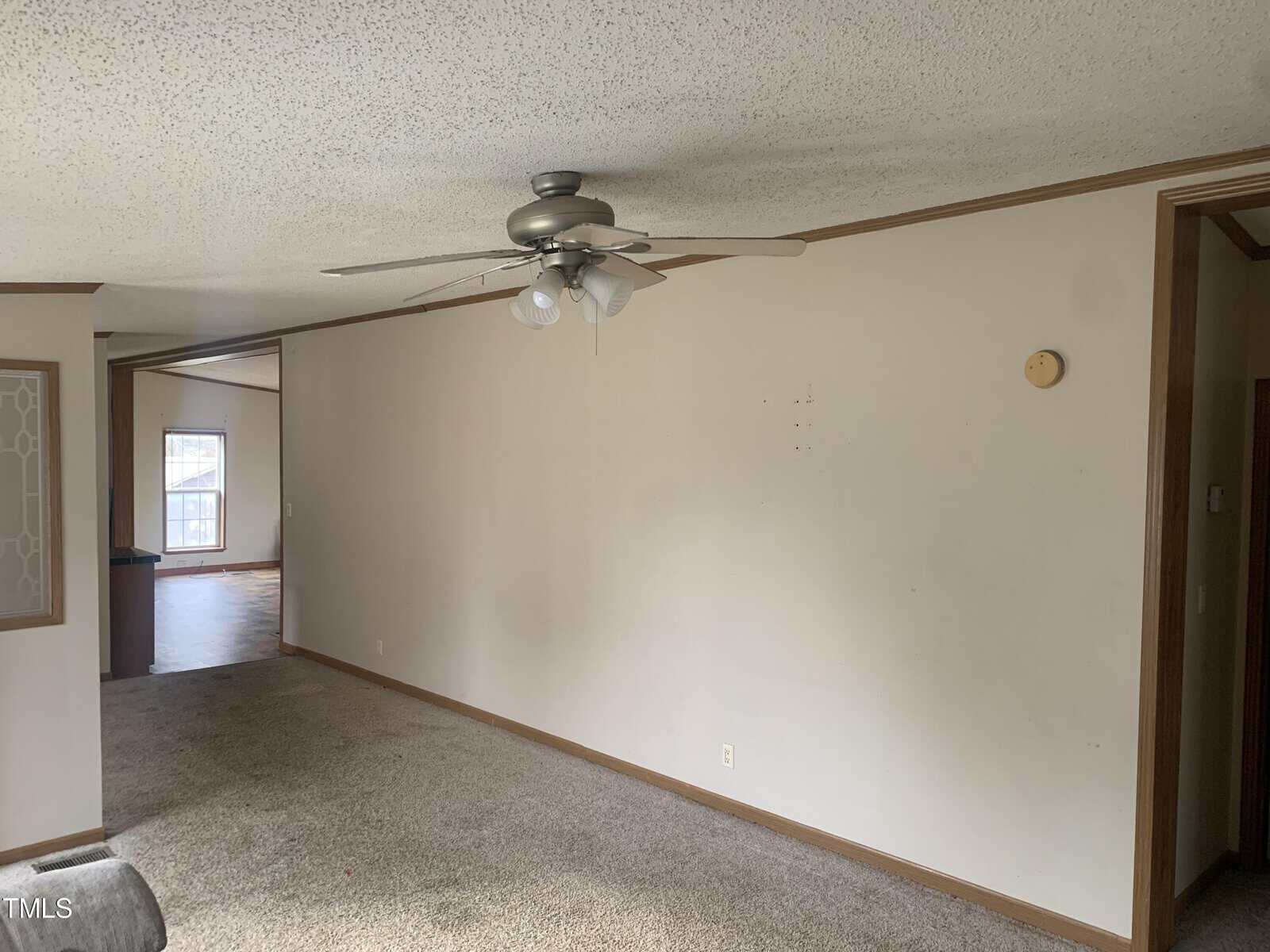 An empty room featuring beige walls, carpeted floor, and a ceiling fan with a light fixture.