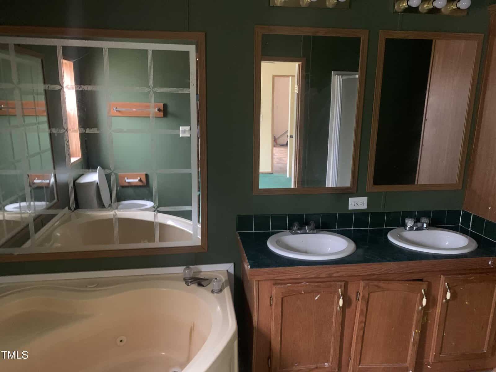 A bathroom featuring a large mirror, dual sinks, wooden cabinets, and a built-in bathtub, with visible reflections of the interior.