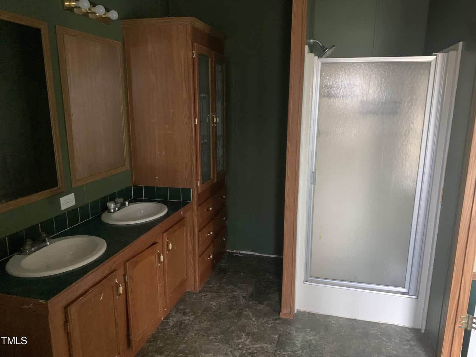 A bathroom with dual vanities, wooden cabinets, and a standalone shower with a frosted glass door.
