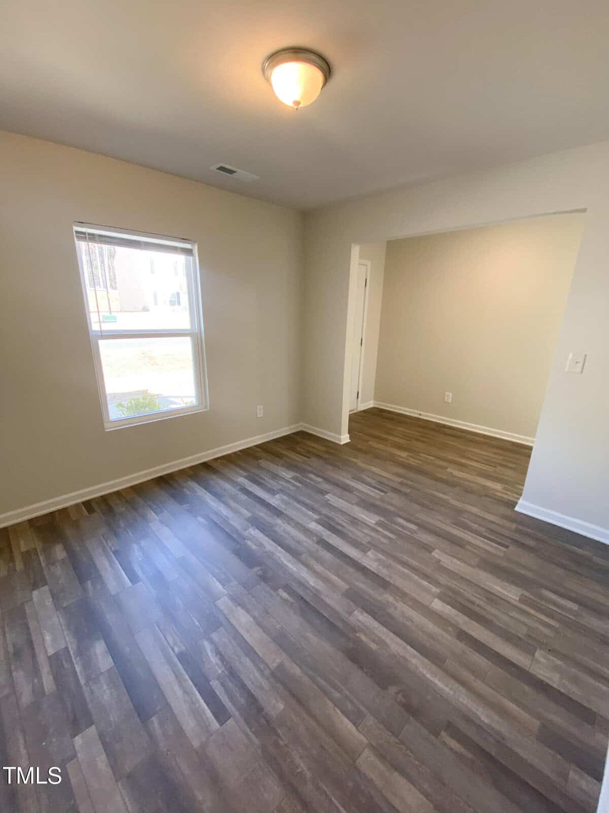 An empty room with beige walls, a window, and laminate wood flooring.