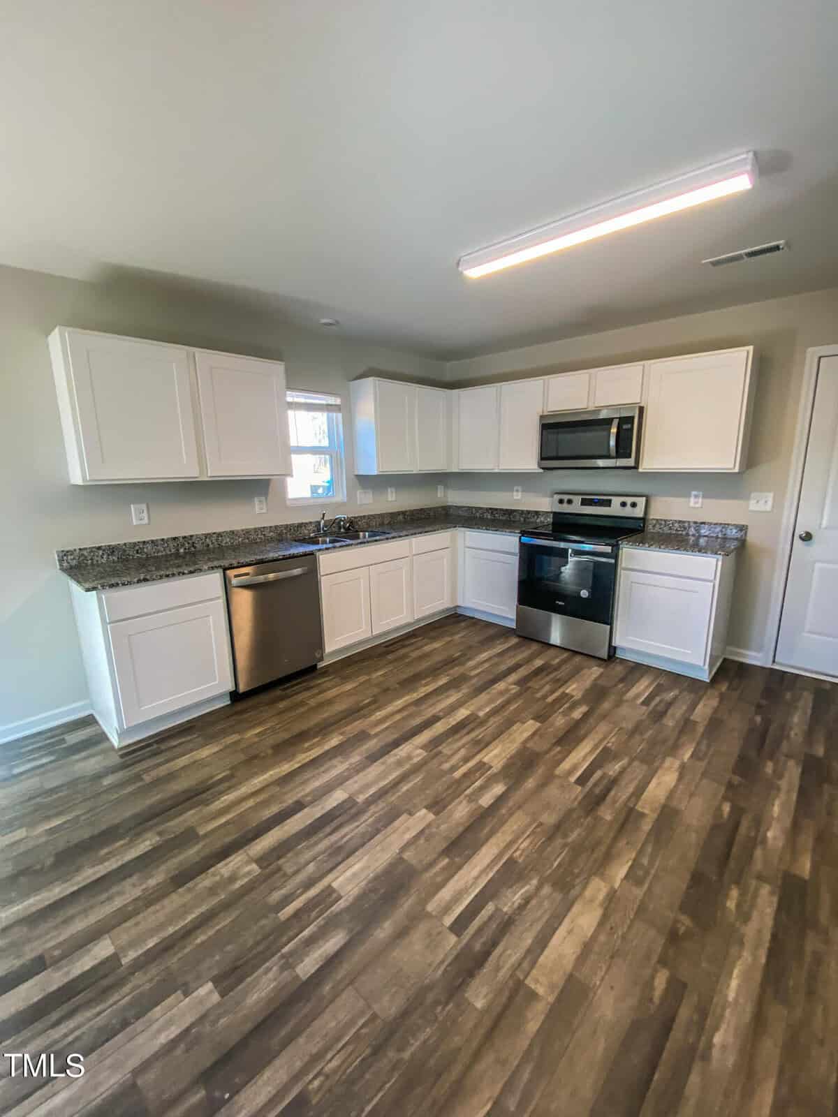 A modern kitchen with white cabinetry, stainless steel appliances, and dark wood flooring.