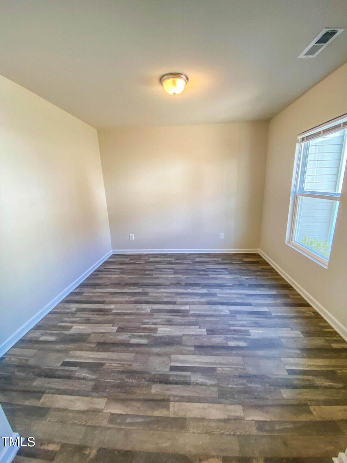 An empty room with beige walls and a window featuring a wood-look laminate flooring.