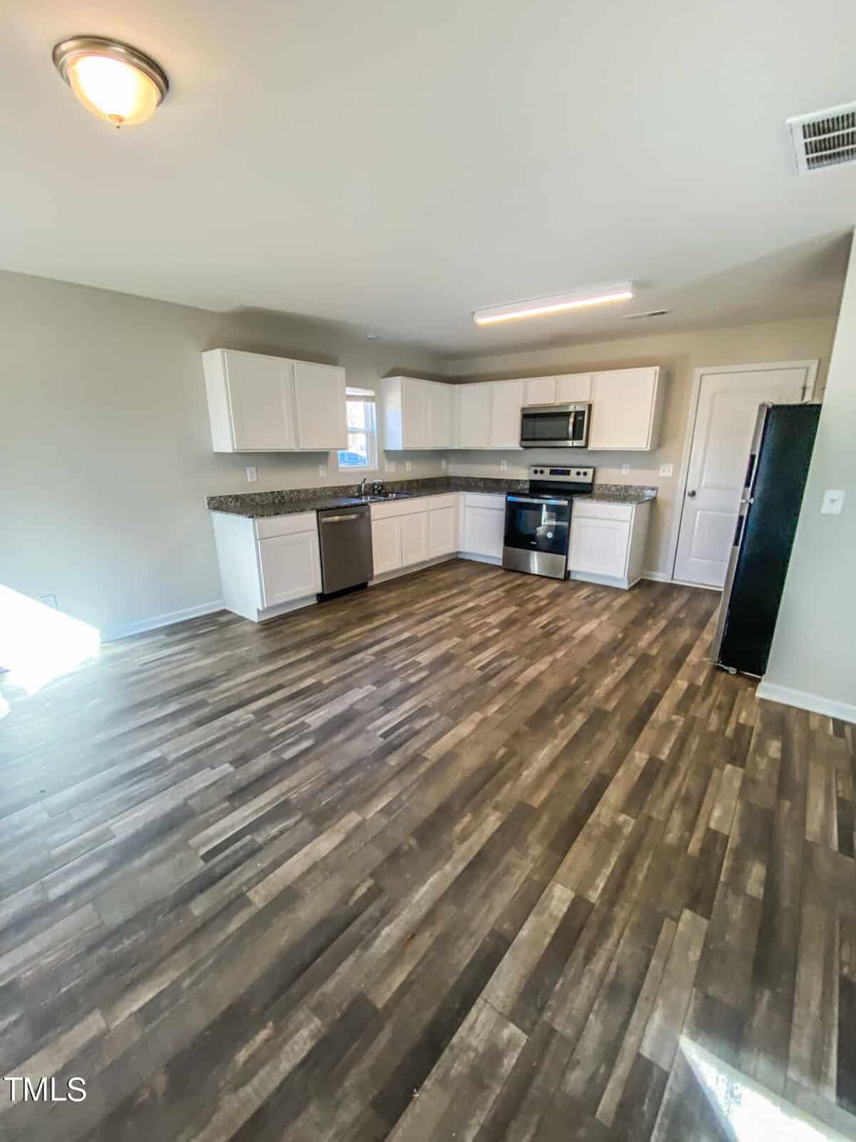 A modern kitchen with white cabinets, stainless steel appliances, and dark wood laminate flooring.