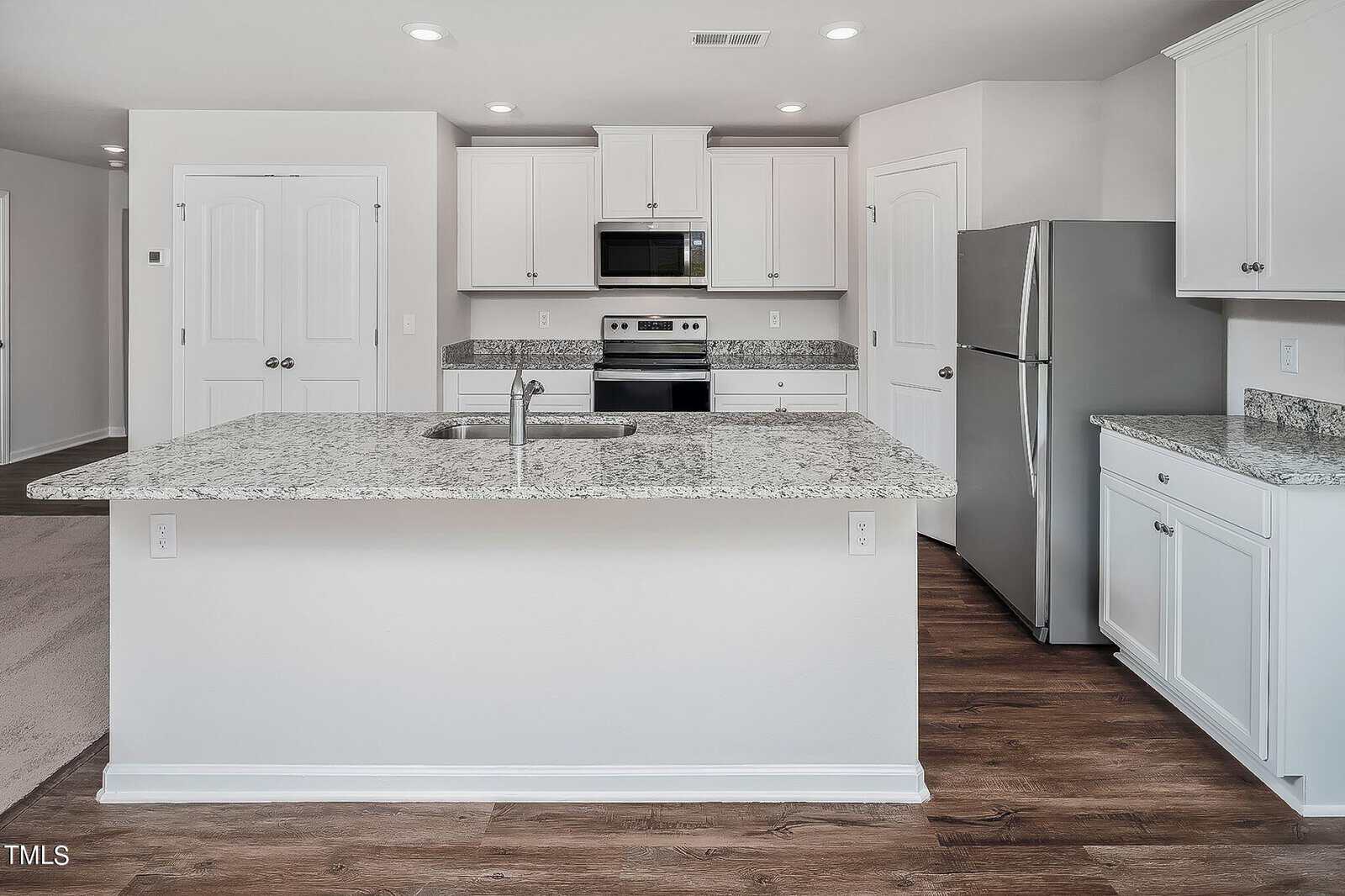Modern kitchen with white cabinets, stainless steel appliances, and granite countertops. Features a central island with a sink, white walls, and wood laminate flooring.