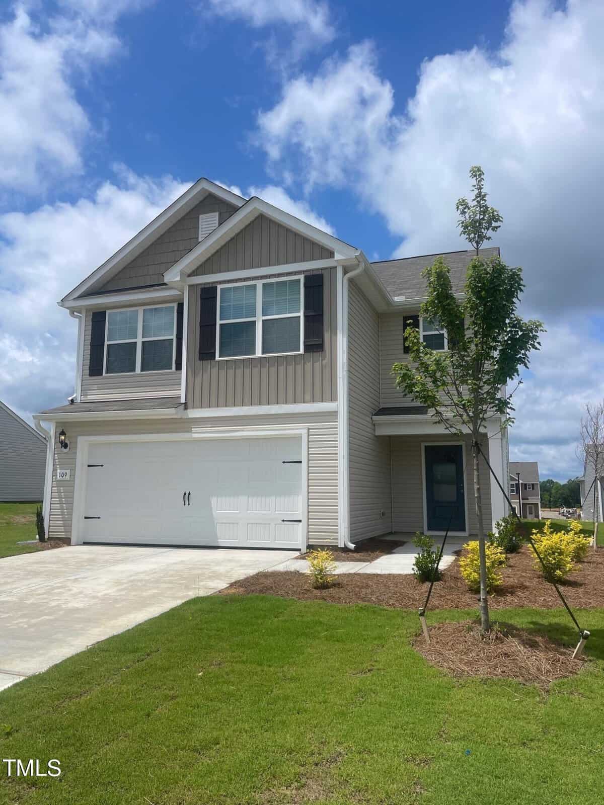 Located at 109 Cultivar Street in Oxford, this two-story modern house boasts beige siding and white trim. It features a two-car garage and a charming front porch. The freshly planted tree and bushes enhance the front yard, while the sky above is partly cloudy with blue patches.