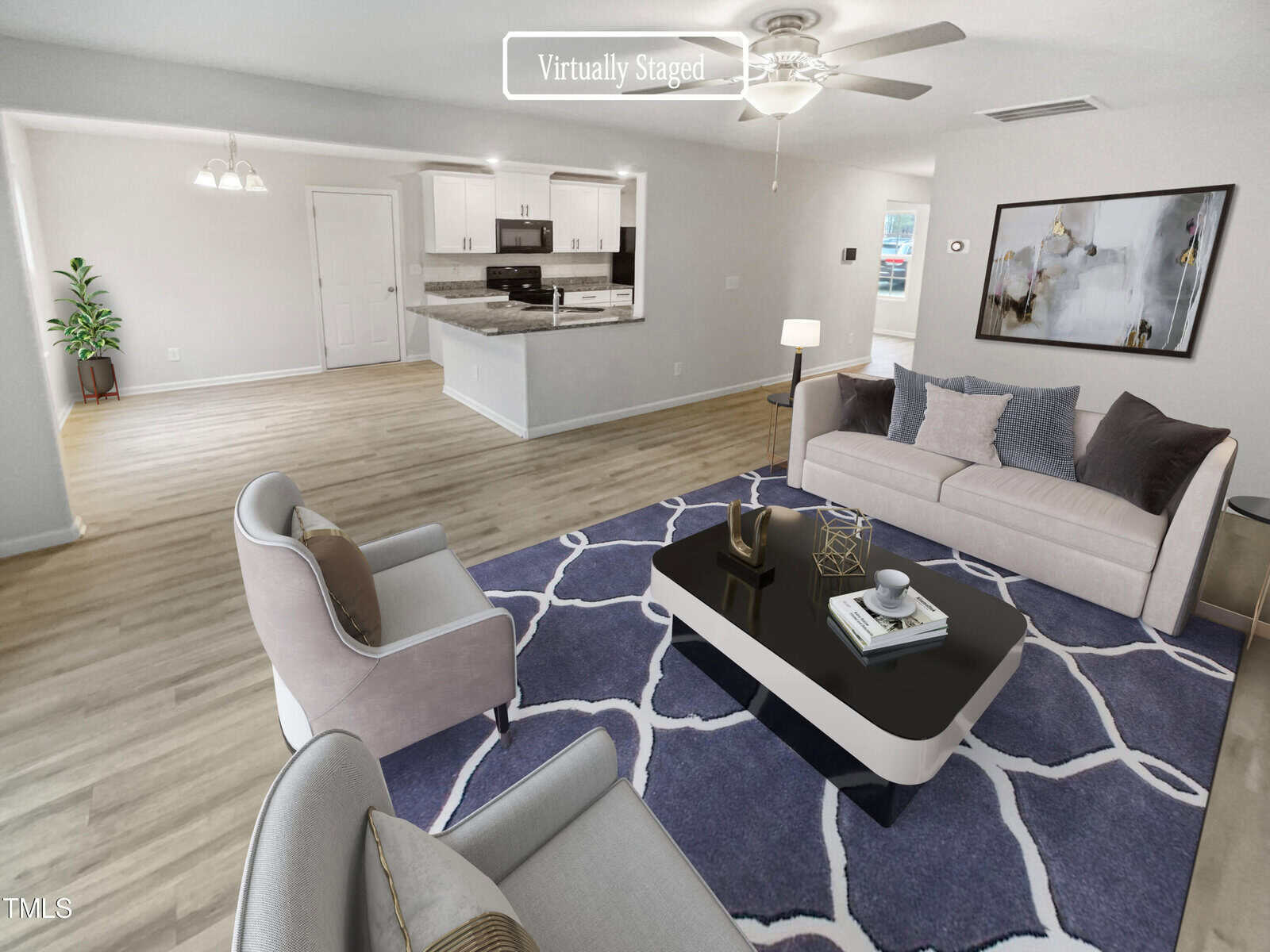 A bright living room with light wood floors, a modern sofa, two armchairs, a black coffee table on a purple rug, and an open kitchen in the background. Text reads "Virtually Staged.