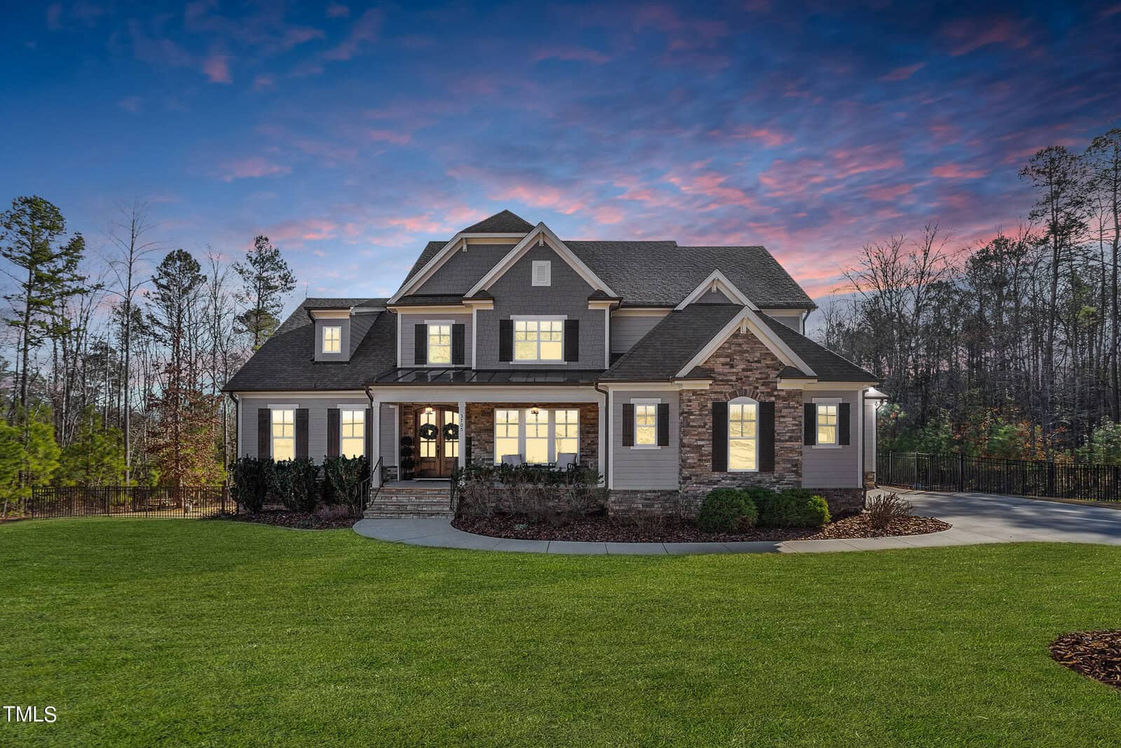 Suburban two-story house at 3705 Dillard Lane with a gabled roof and stone facade, warmly lit windows against a twilight sky. Nestled in serene Wake Forest, it is surrounded by manicured lawns and trees, creating an inviting atmosphere.