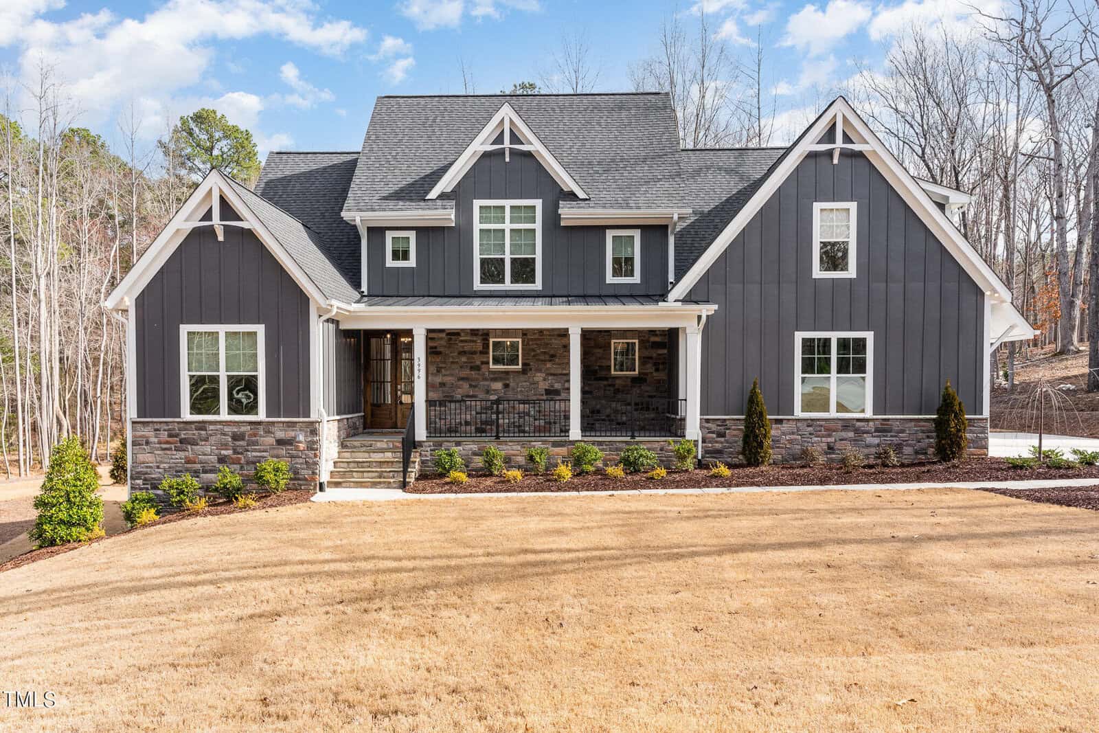 Located at 3996 Cashmere Lane, Youngsville, this modern two-story house boasts dark gray siding and stone accents, complemented by a large front porch. The yard is beautifully landscaped with small shrubs and trees, while the sky above remains partly cloudy.